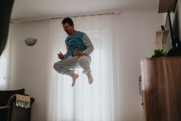 A vibrant and energetic young man jumps joyfully inside a modern, well-lit living room, expressing...