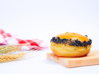 Tasty doughnut with yellow glaze and dark crumb topping, presented on a wooden board with wheat stalks and red checkered cloth in a clean, white background
