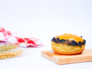 Tasty doughnut with yellow glaze and dark crumb topping, presented on a wooden board with wheat stalks and red checkered cloth in a clean, white background
