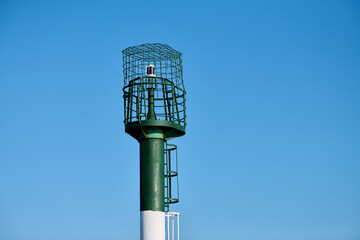 Solitary green metal lighthouse stands tall against clear blue sky, evoking tranquility at coastal locations with its sturdy structure and navigational purpose