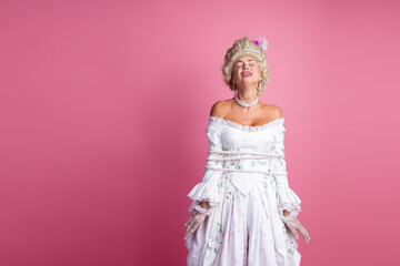 Elegant woman tied with rope dressed in a baroque inspired gown posing against a pink background