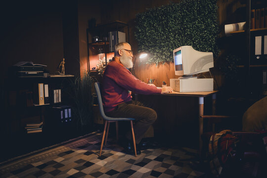 Senior programmer working on a vintage computer in a cozy home office, showcasing experience and dedication to technology