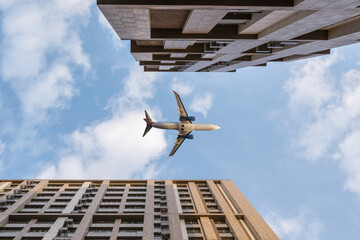 Bottom view of tall multi-story buildings against blue sky and flying passenger plane
