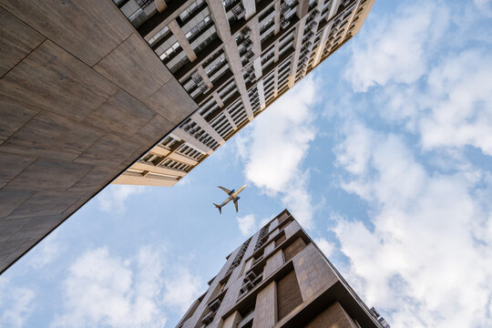 Bottom view of tall multi-story buildings against blue sky and flying passenger plane