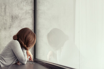Beautiful сaucasian young woman standing near big panoramic window and looking at mobile phone.