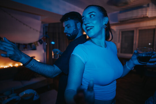 Two young adults are captured dancing joyfully at a lively birthday party. The atmosphere is illuminated by blue lighting, enhancing the festive and celebratory mood of the event. - Powered by Adobe