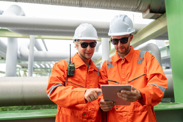 Two male petrochemical engineers with walkie-talkie and tablet working and discussing inspection...