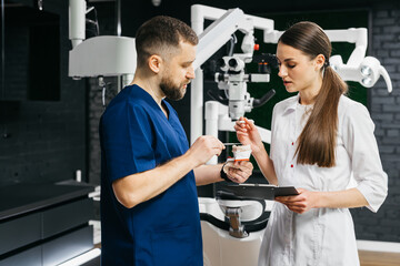 In a modern dental clinic, the doctor and nurse discuss the details of treatment by analyzing the diagnosis on a model of the jaw. Concept of dental services and treatment.