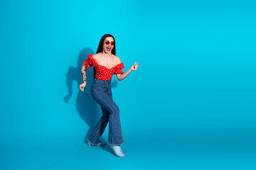 Young woman in red top and denim poses playfully against blue background with joyful expression