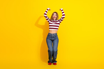Cheerful young woman in casual striped pullover posing energetically against a vibrant yellow backdrop.