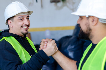 Factory workers shaking hands.Friendly industry workers at construction site wearing safety hats