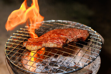 A thick, juicy steak sizzles on a hot grill as flames rise beneath it — capturing the intense heat and flavor of open-fire cooking