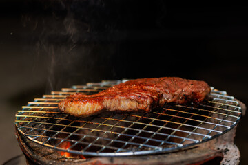 A thick, juicy steak sizzles on a hot grill as flames rise beneath it — capturing the intense heat and flavor of open-fire cooking
