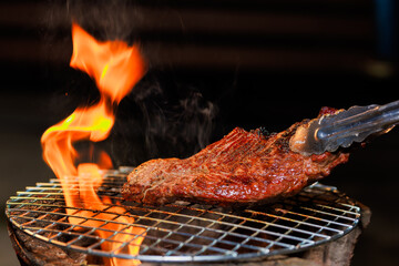A thick, juicy steak sizzles on a hot grill as flames rise beneath it — capturing the intense...