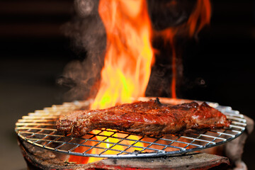 A thick, juicy steak sizzles on a hot grill as flames rise beneath it — capturing the intense...