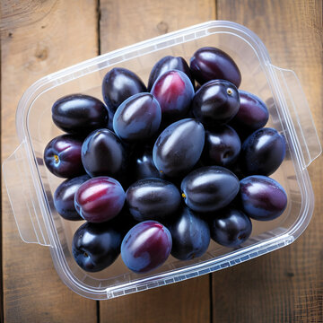 Ripe prune plums in a clear plastic container. Fresh fruit and a subspecies of Prunus domestica, a freestone fruit, also called European plum or Zwetschge, with a purple, violet and black skin. Photo.
