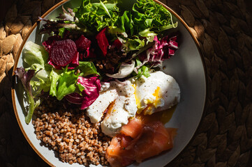 Homemade healthy and balanced breakfast from buckwheat, smoked salmon, salad leaves, beetroot, and poached eggs. Breakfast with strong sun light and shadows
