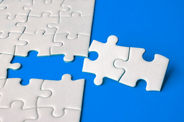 Fototapeta premium Close up view of missing white jigsaw puzzles, symbol of partnership and unity on blue background