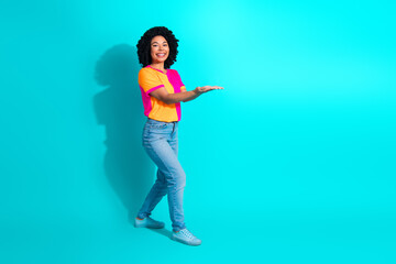 Happy young woman in colorful casual outfit presenting with a smile against a vibrant turquoise background for advertising.