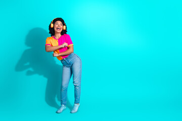 Cheerful young woman dancing in colorful outfit with headphones on turquoise background exuding happiness and positive energy