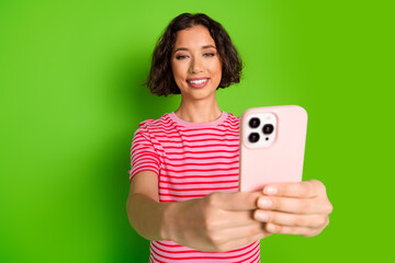 Smiling Young Woman Taking a Selfie with a Smartphone in a Pink Case Against a Vibrant Green...