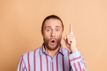 Surprised young man pointing upward with enthusiasm wearing a striped shirt in front of a beige...