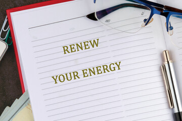 A planner opened to a page featuring the phrase renew your energy. A pen and glasses rest on the planner, suggesting a focus on personal growth and productivity during a productive day