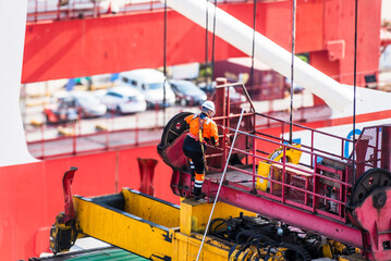 Stevedore descending onto a container ship from a large crane spreader to unlock containers before...