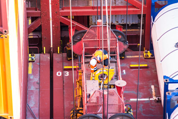 Stevedore descending onto a container ship from a large crane spreader to unlock containers before...