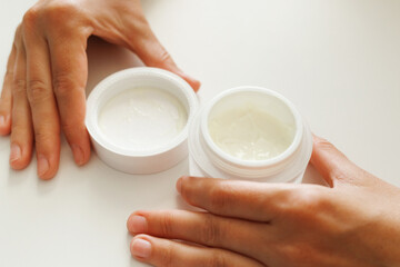 Hands open a jar of white cream, revealing the product inside. Skincare and beauty routine focus.