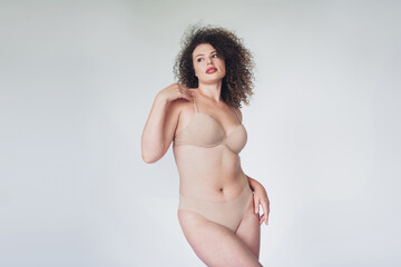 Confident plus size woman modeling lingerie with natural beauty and curly hair on a neutral...