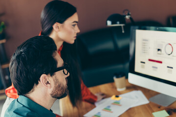 Focused coworkers collaborating on business analytics in a modern workspace, analyzing data graphs and charts on a desktop computer