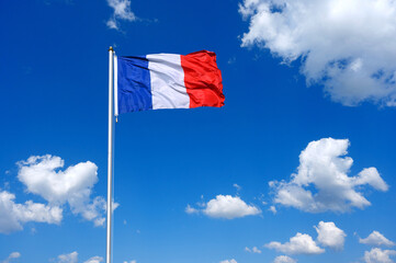 The flag of  France flutters in the wind in a blue sky with white clouds