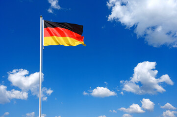 The flag of  Germany flutters in the wind in a blue sky with white clouds