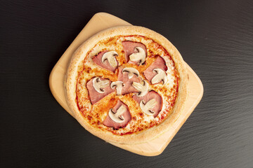 Classic Ham & Mushroom Pizza – A freshly baked pizza topped with savory ham, sliced champignons, tomato sauce, and melted cheese on a golden crust. Shot from above on black stone.