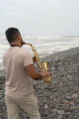 Saxophonist playing on beach seeking inspiration from ocean waves