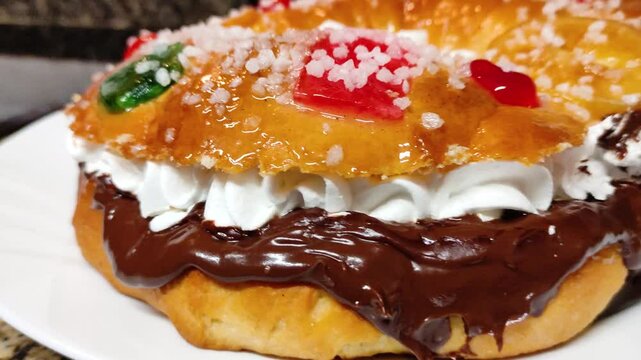 Delicious traditional Spanish Rosc&oacute;n de Reyes dessert in close-up, filled with cream and chocolate with colored jelly pieces and powdered sugar on top.