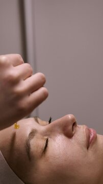 The beautician applies vitamin C serum with antioxidants against pigmentation and wrinkles to a woman's face. Professional care in a beauty salon
