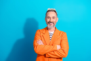 Smiling charismatic middle aged man in an orange suit posing confidently with crossed arms against a bright blue background