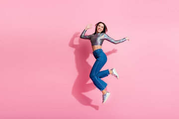 Happy young woman in stylish shiny top and jeans jumping against a vibrant pink background