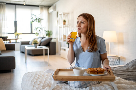 Woman enjoying breakfast in bed with orange juice and waffles