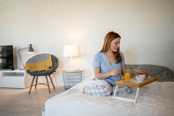 Woman enjoying breakfast in bed in cozy bedroom