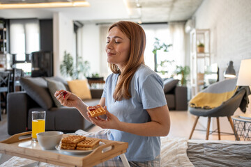 Woman enjoying waffles with jam for breakfast in bed