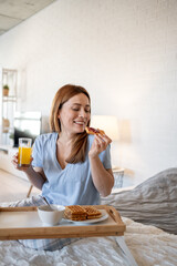 Woman enjoying breakfast in bed with waffles and orange juice