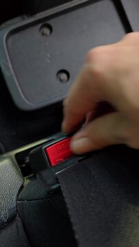 Hand buckling and unbuckling car seatbelt closeup. Vertical video showing a hand fastening and releasing a car seatbelt. red PRESS button and seatbelt mechanism inside a passenger vehicle.