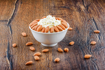 Almonds on a bowl with cottage cheese and on a wooden background.