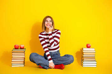 Young woman in a striped top sitting cross legged on yellow background surrounded by apples and book