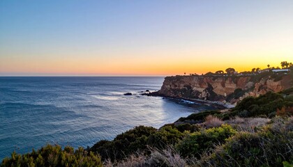 Coastline view cliffs, ocean, & greenery at sunset, sky gradient pink to yellow, calm water