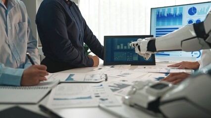 A business team engages in a meeting featuring artificial intelligence technology. Interactive charts and graphs are displayed, showcasing data analysis in a modern office setting.Noogenesis