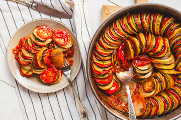 Homemade ratatouille preparation and serving. Child's hands placing vegetable slices into a baking...